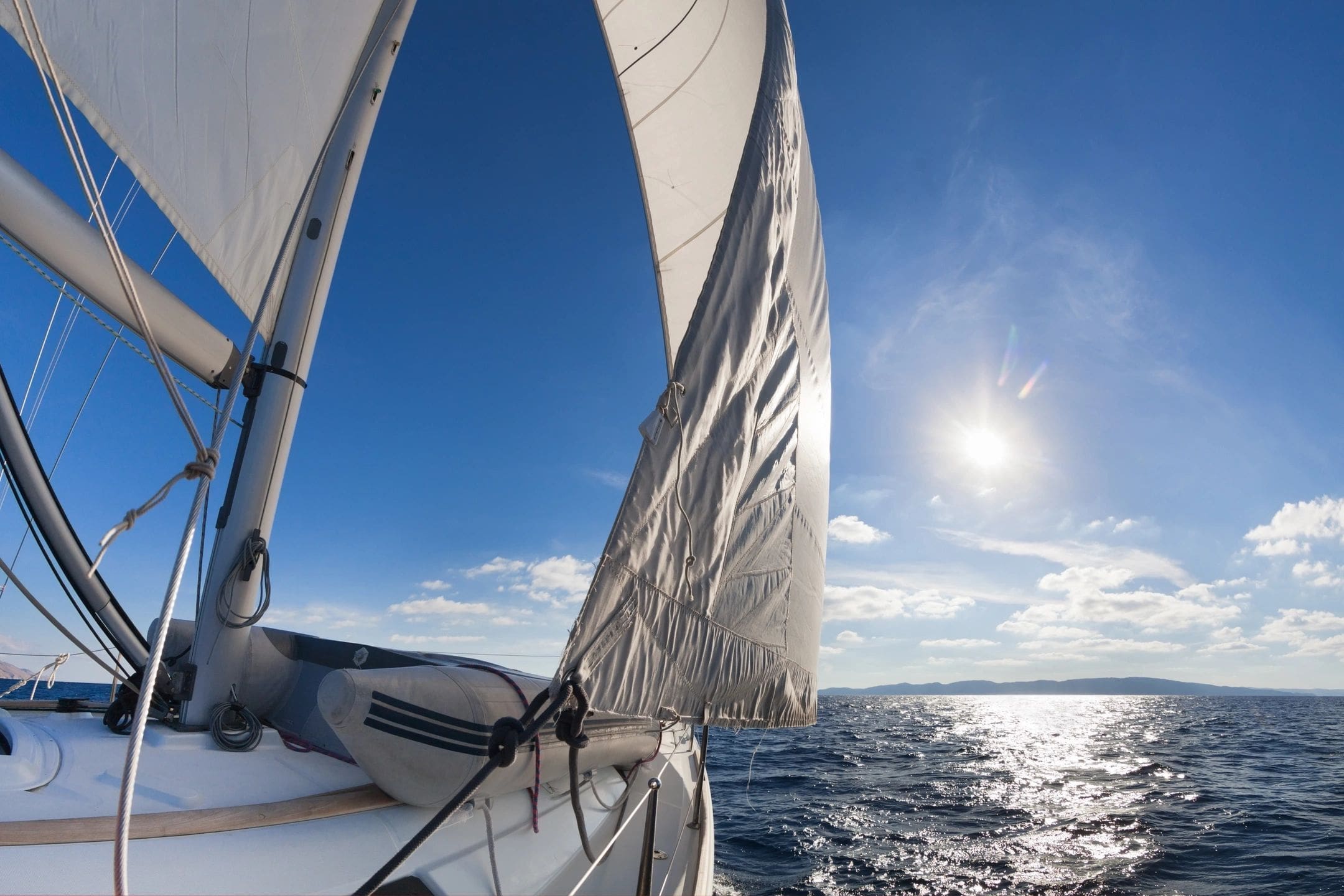 A sail boat sailing on the ocean under a blue sky.